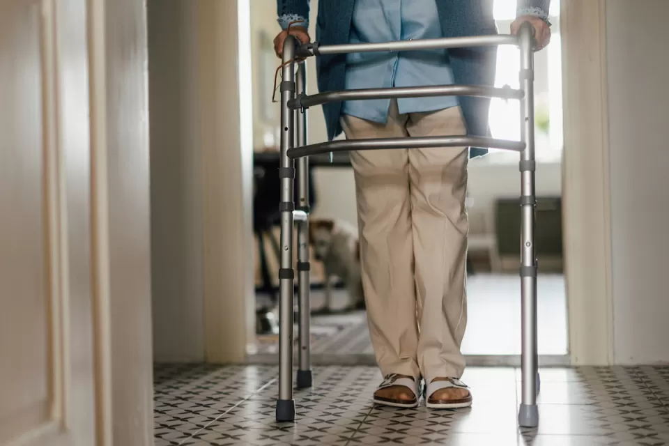 Close-up of elderly person walking inside home leaning on walker.